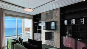 Ein modernes Wohnzimmer mit großem Fenster mit Blick aufs Meer, einer schwarzen Unterhaltungsecke und einem grünen Sofa.