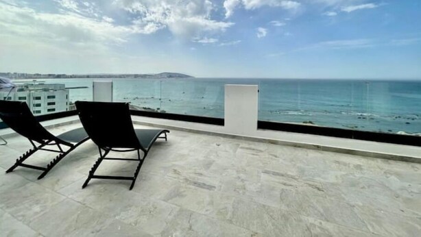 Ein Balkon mit zwei schwarzen Liegestühlen, der Blick geht auf die Stadt und das Meer.