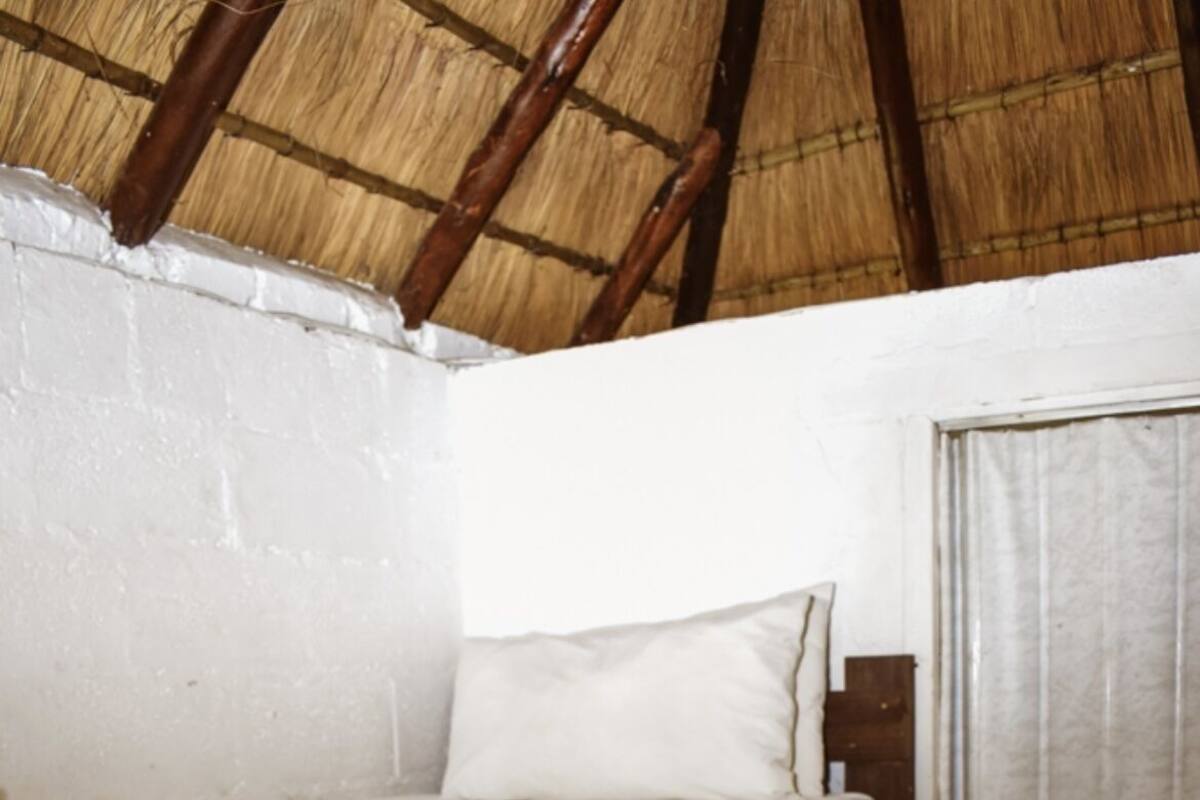 Una cama litera con ropa de cama blanca y una colcha roja, un cabecero de madera y una puerta con cortina.