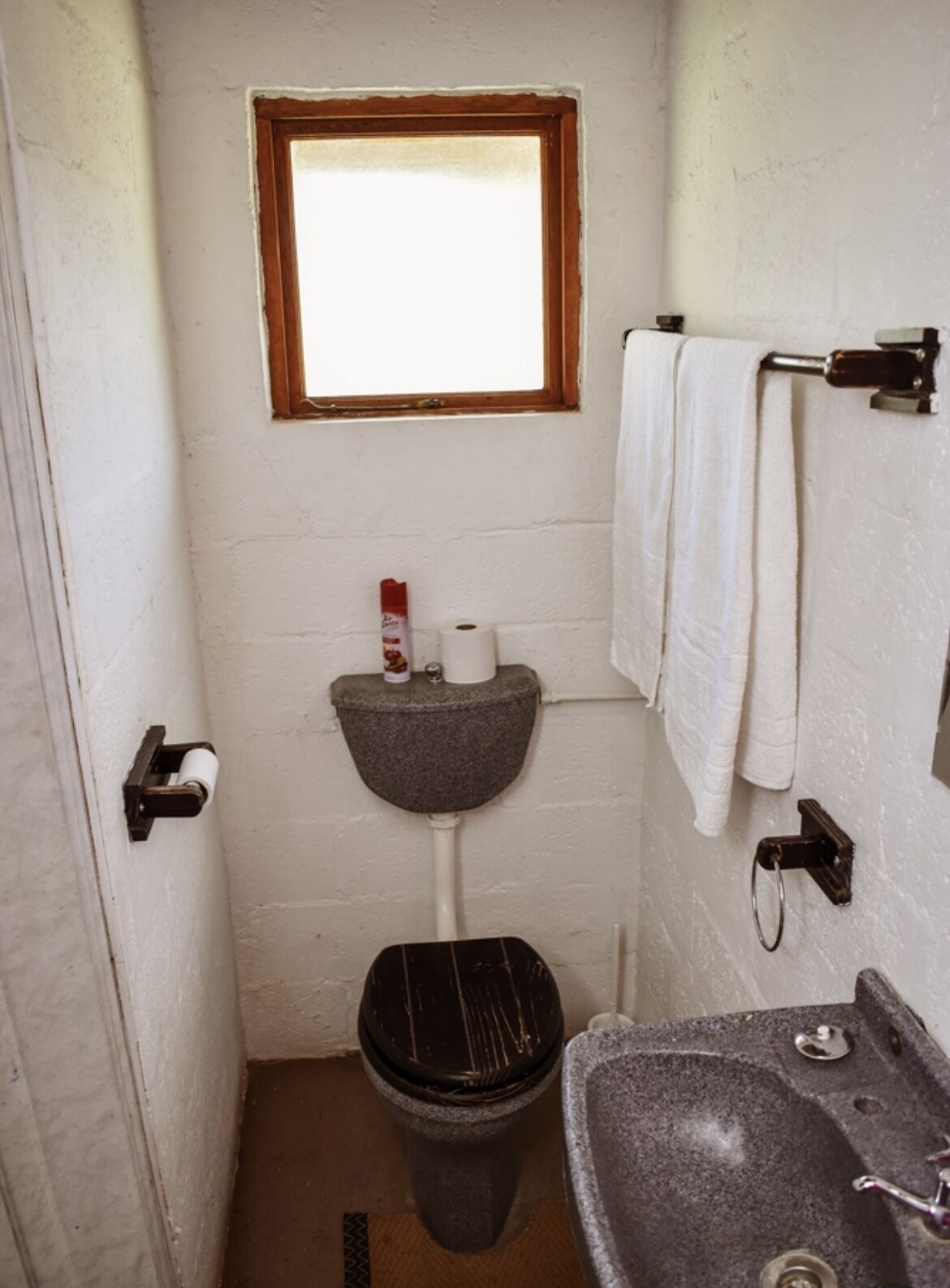 Et lille badeværelse med vindue, toilet, håndvask og håndklædetørrestativ.