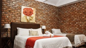 A hotel room with a brick wall, a large bed with white bedding, two bedside tables with lamps, and a red rose painting on the wall. - Roydon Reserve (Komani)