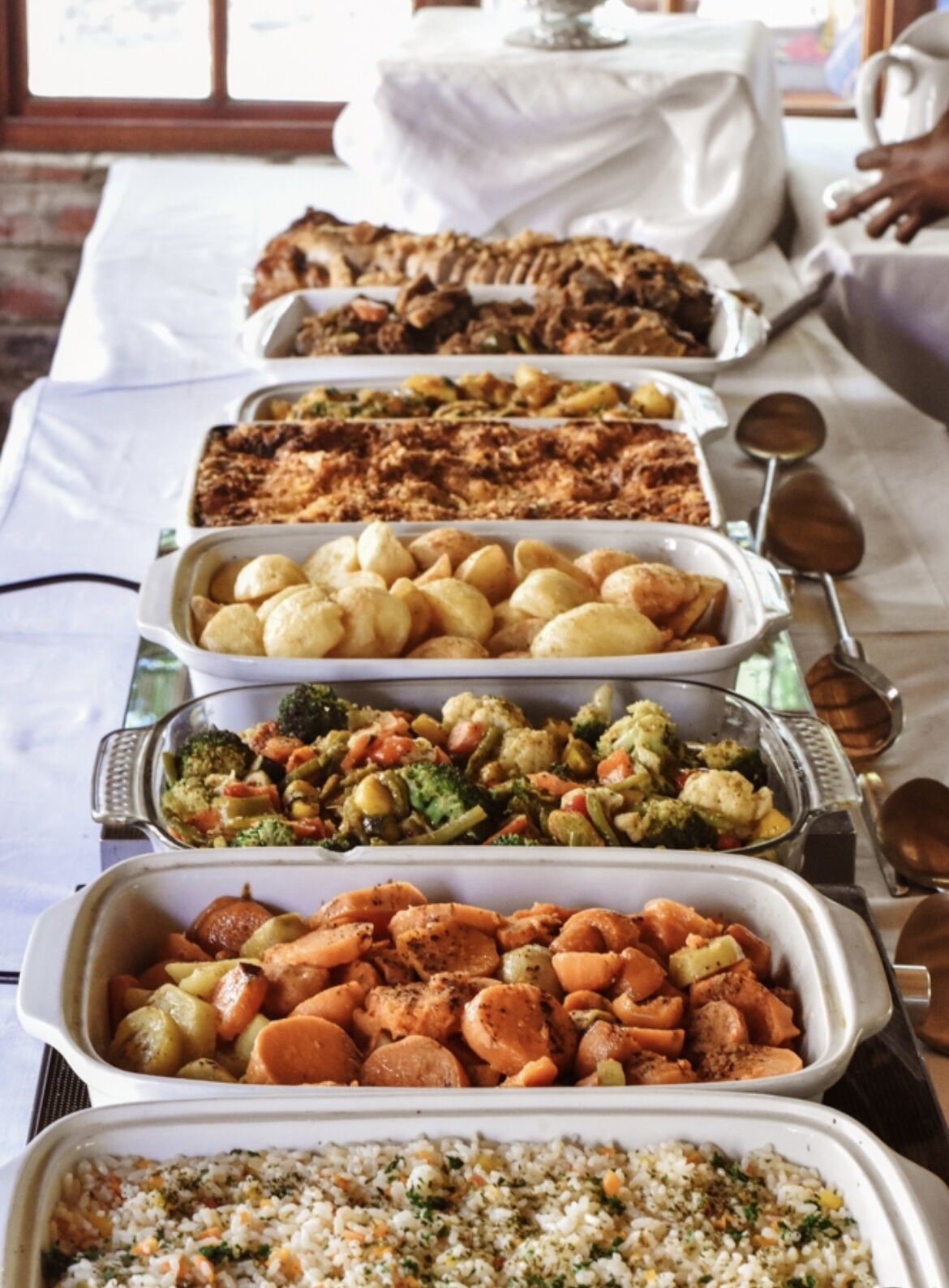 A buffet table with various dishes including roasted meats, potatoes, vegetables, and rice.