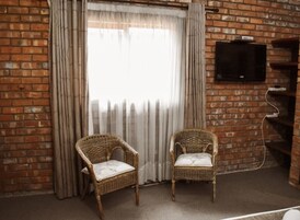 Una habitación con paredes de ladrillo, dos sillas de mimbre, un televisor montado en la pared y una ventana con cortinas.