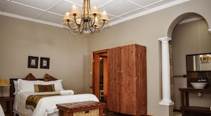 A bedroom with a bed, wooden wardrobe, chandelier, and a bathroom with a sink and mirror. - Roydon Reserve (Komani)