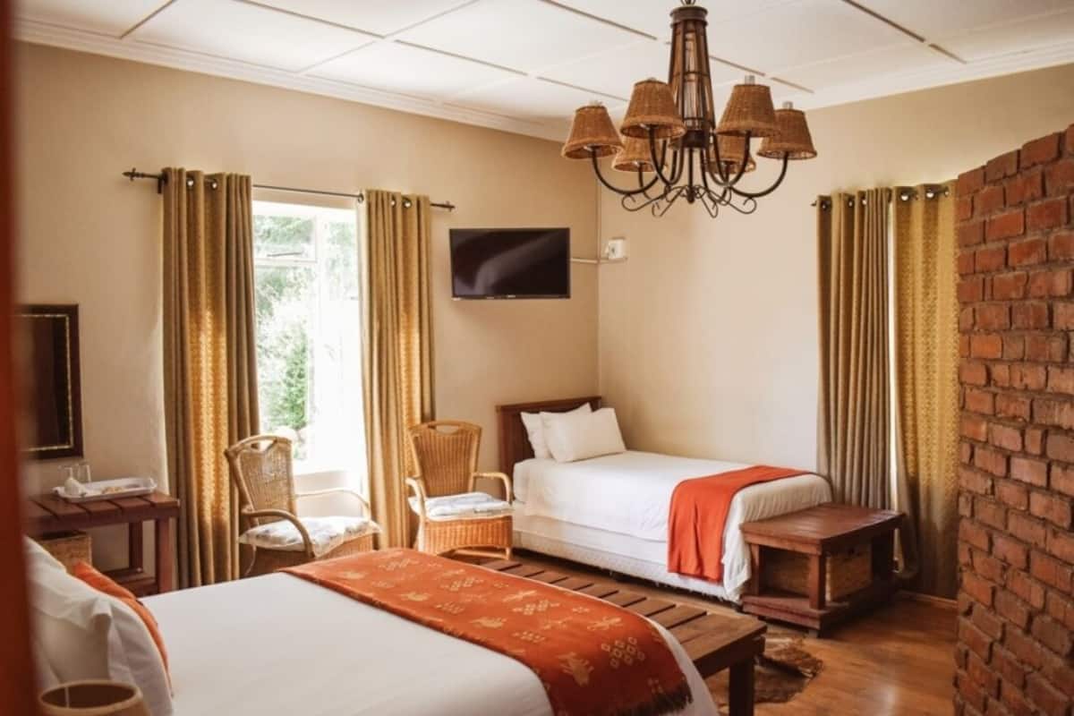 Una habitación de hotel con dos camas, un televisor, una silla de mimbre y una pared de ladrillo.