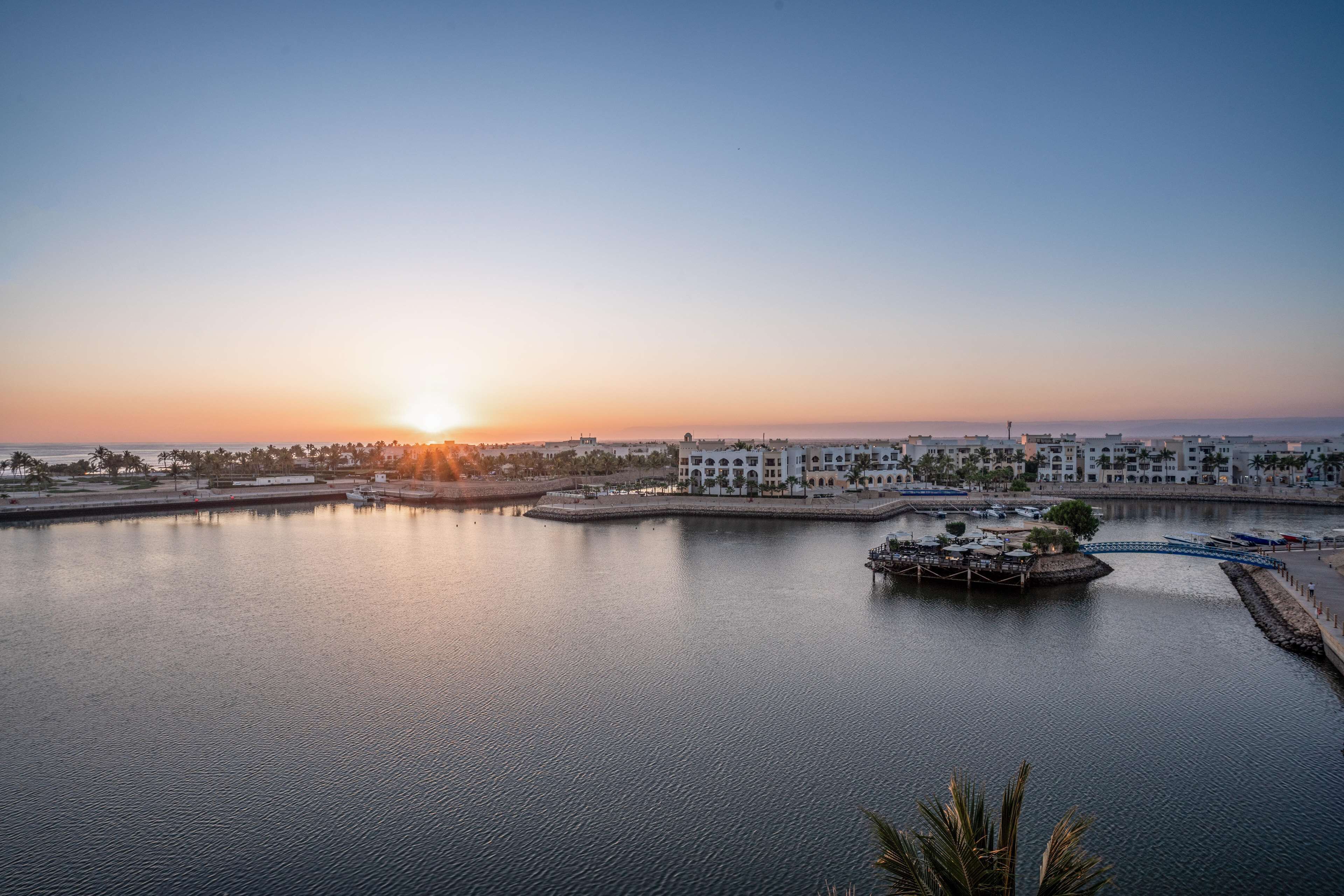 Un puerto deportivo con barcos amarrados, un paseo marítimo y edificios al fondo.