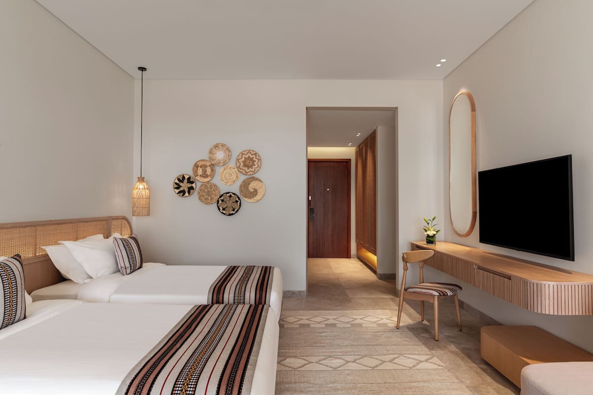 A modern hotel room with two beds, a TV, a desk, and decorative wall art.