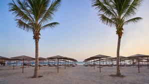 A beach with palm trees and beach umbrellas. - The Club by Fanar (Salalah)