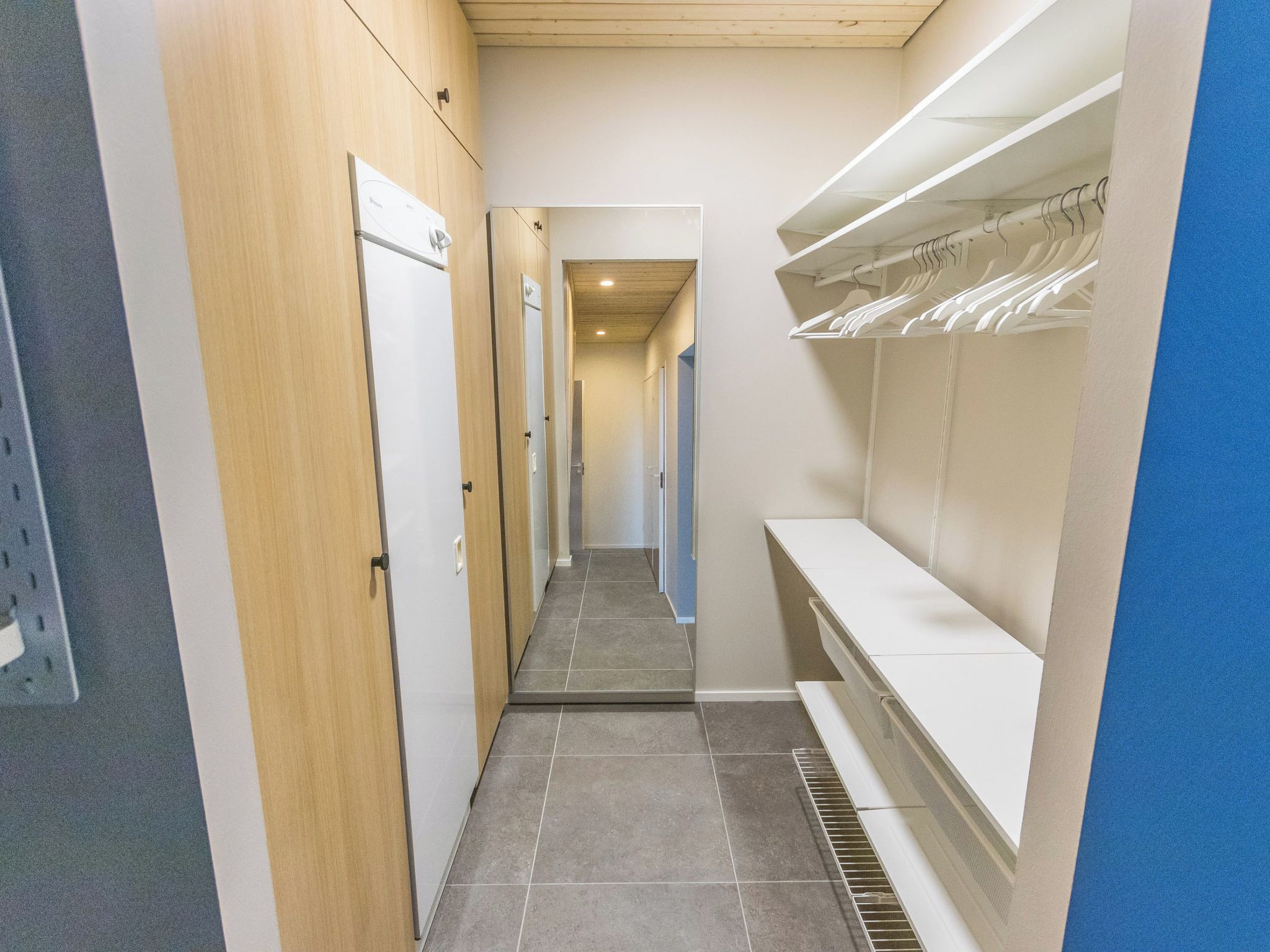 A narrow hallway with a tiled floor, wooden walls, and a white door on the left.