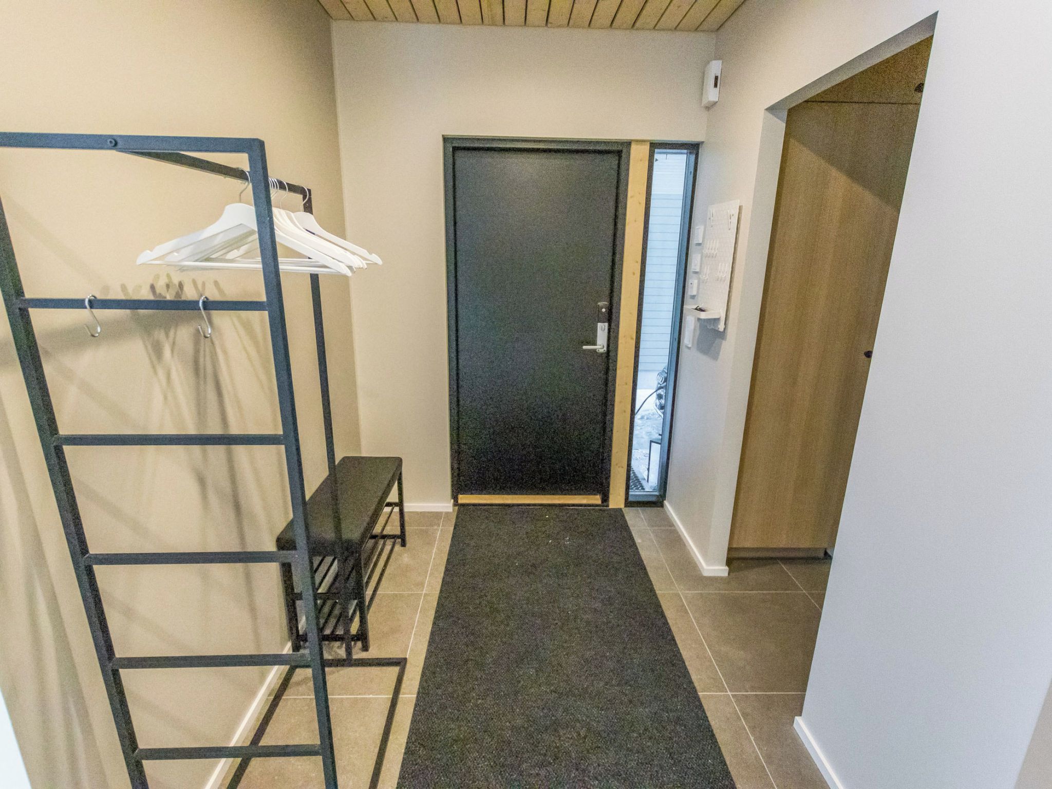 A hallway with a black door, a bench, and a clothes rack with hangers.