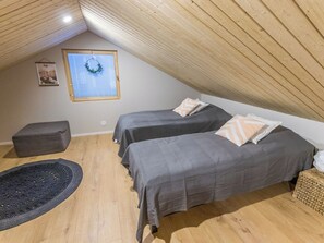 A small, cozy attic bedroom with two beds, a window with a wreath, and a wooden ceiling.