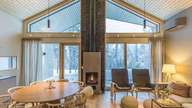 A spacious living area with a large wooden table, comfortable seating, a fireplace, and large windows offering a view of a snowy landscape.