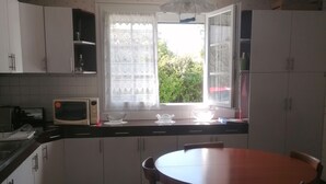 A kitchen with white cabinets, a microwave, a window with lace curtains, a wooden table, and chairs.