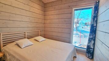 A bedroom with a wooden slatted headboard, two pillows, a bed with a white bedspread, and a window with a view of a snowy landscape.