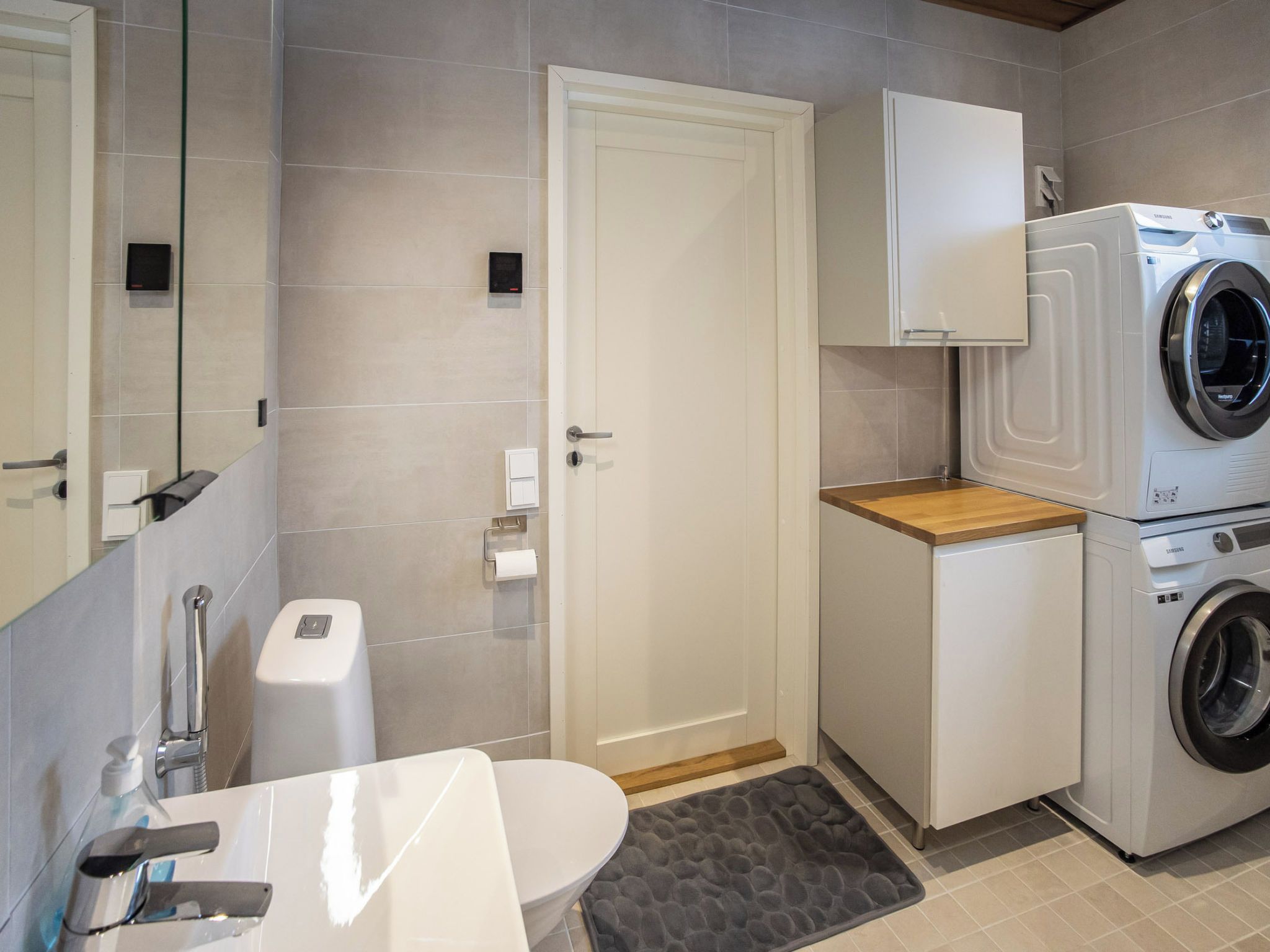 Une salle de bain moderne équipée d’un lave-linge intégré, de toilettes, d’un lavabo et d’un miroir.