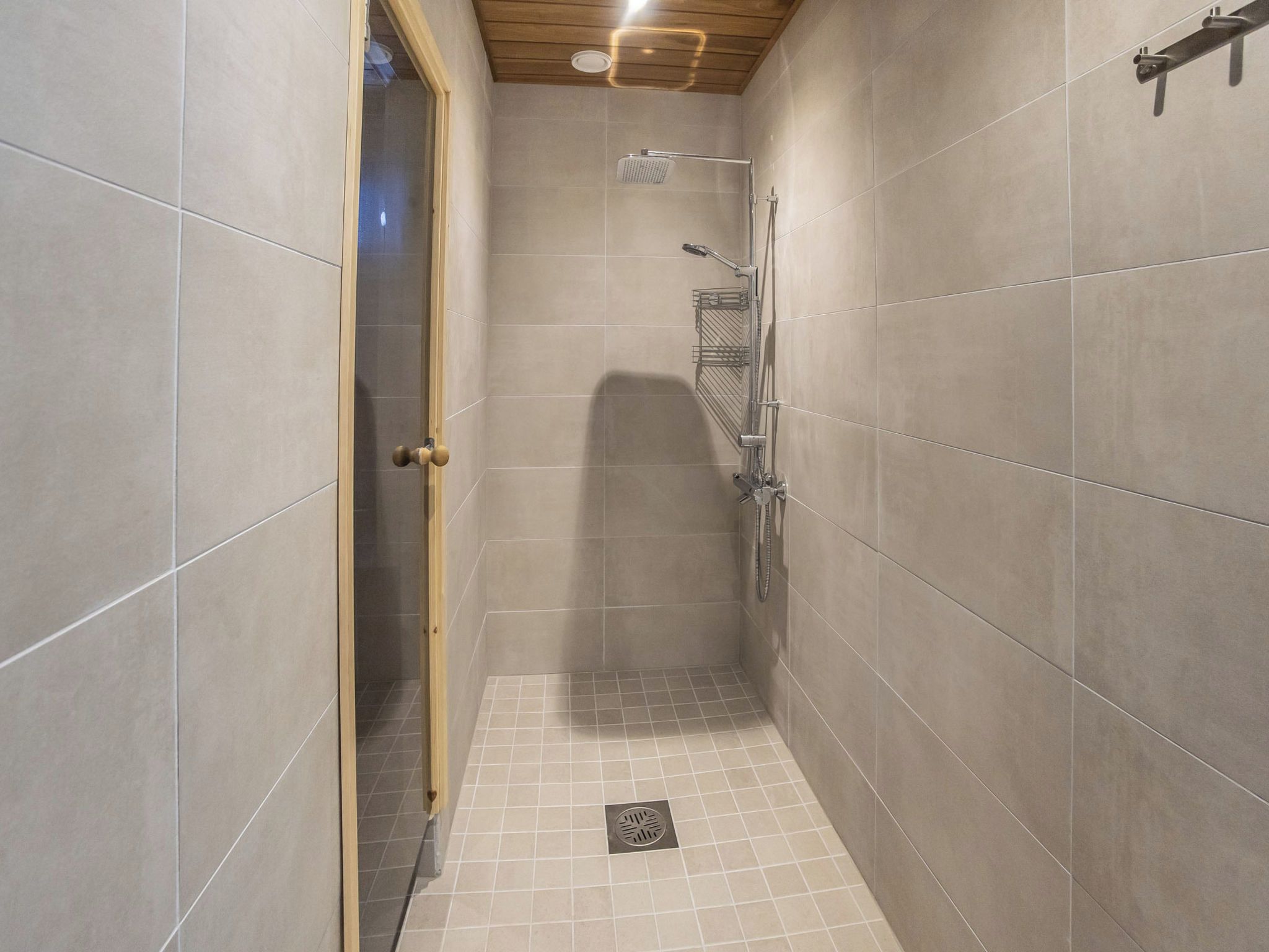 Un petit espace de douche carrelé, équipé d’un pommeau de douche, d’un flexible de douche et d’une étagère en métal.