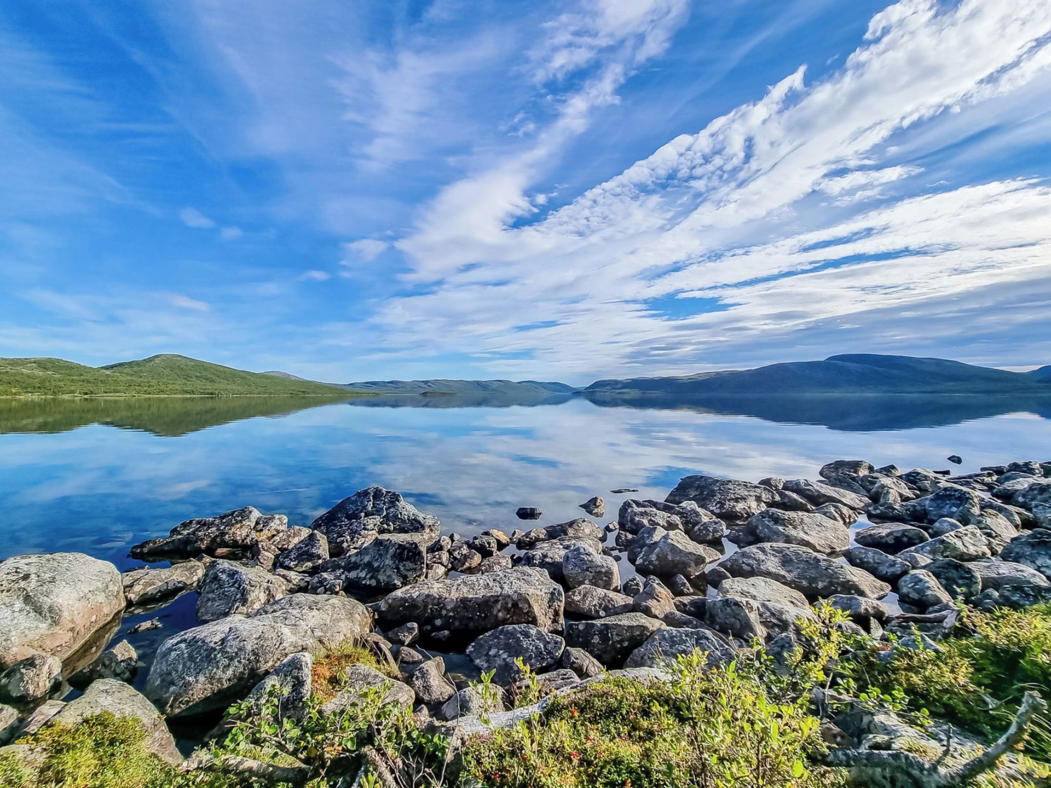Un lac paisible, bordé d’une rive rocheuse et entouré de collines lointaines.