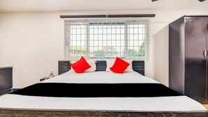 Une chambre à coucher avec un lit, deux oreillers rouges, une fenêtre avec des barreaux et une armoire.