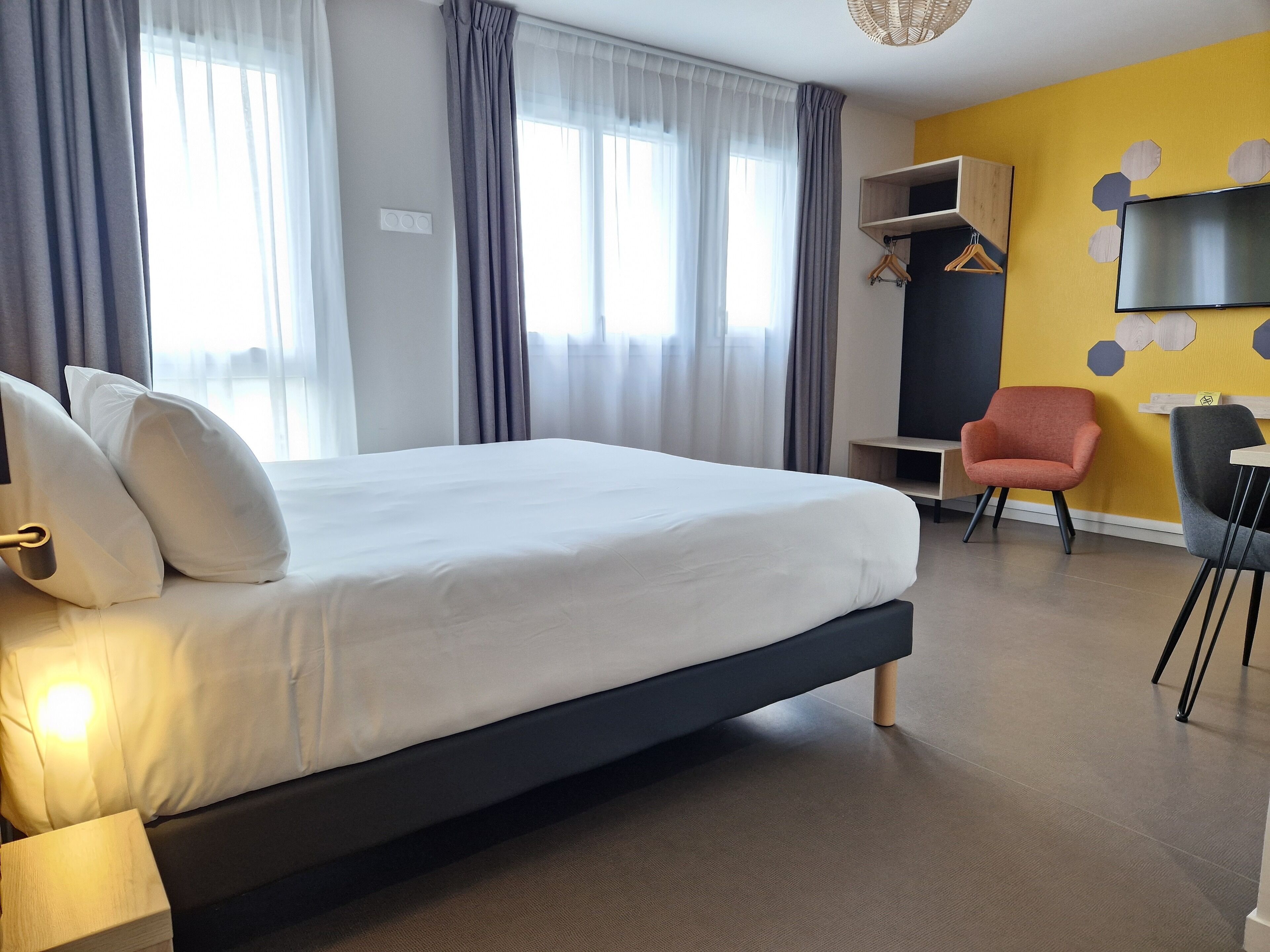 Una habitación de hotel moderna con una cama grande, un escritorio, una silla y un televisor en la pared.