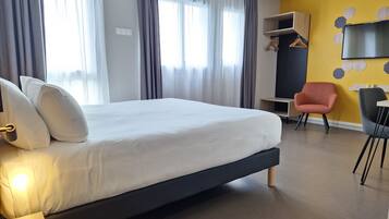 A modern hotel room with a large bed, a desk, a chair, and a TV on the wall.