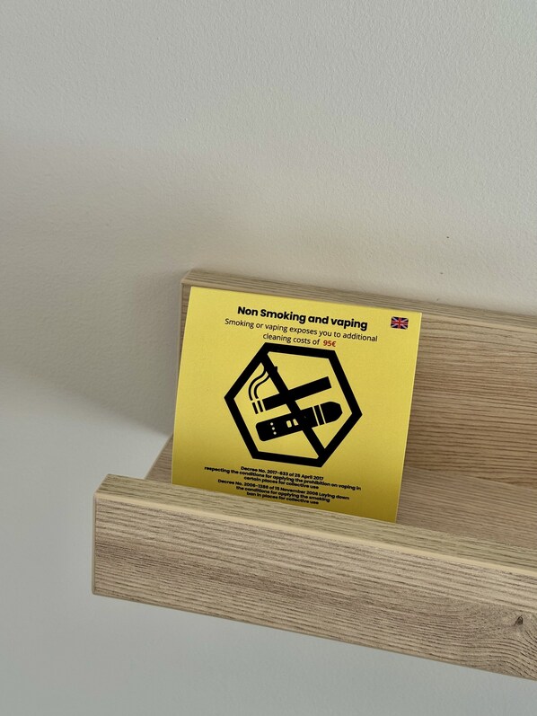 Un letrero amarillo en un soporte de madera que indica 'No fumar y vapear', con información adicional sobre las prohibiciones de fumar y vapear y los costos correspondientes.