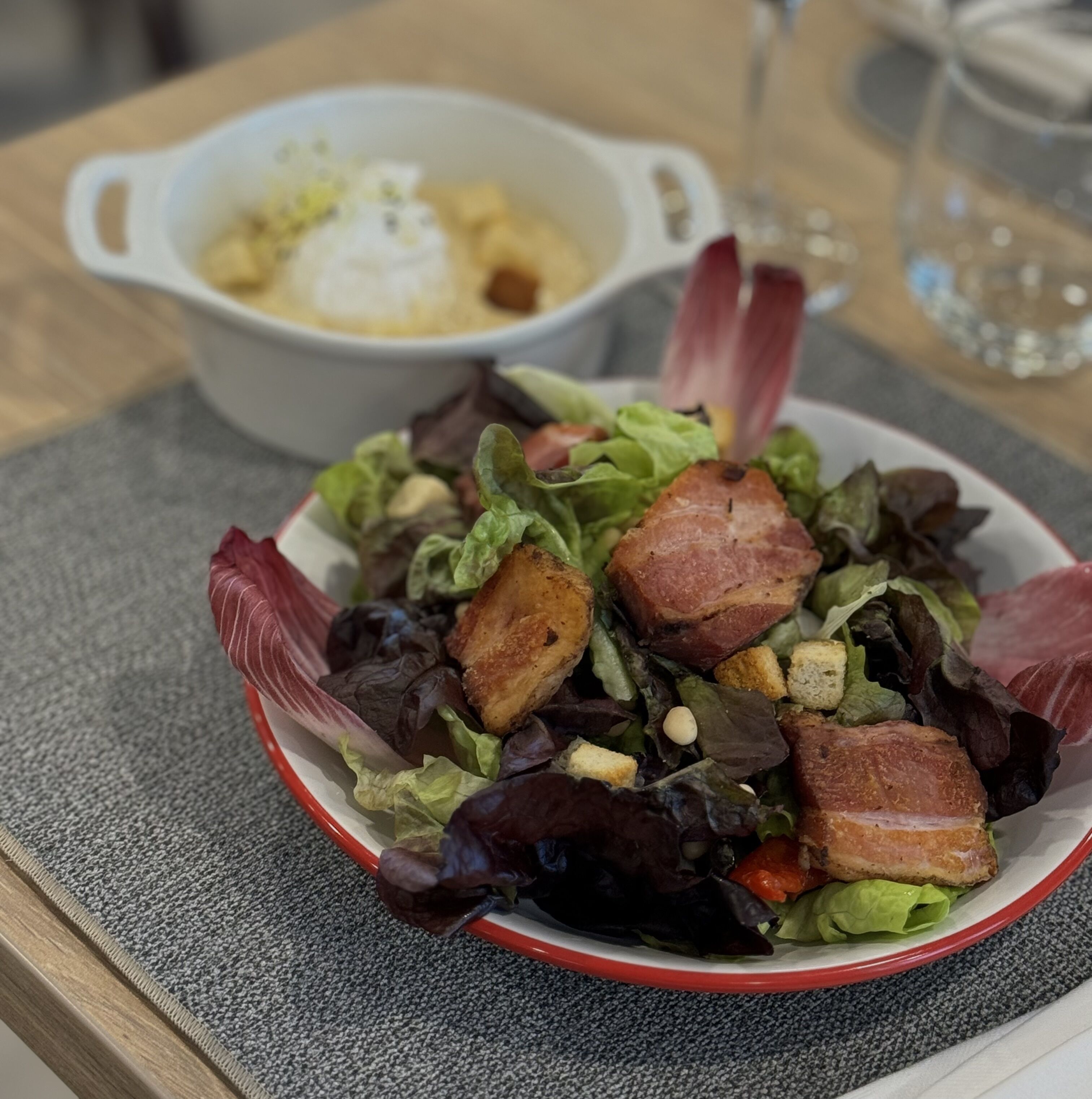 A bowl of salad with croutons and bacon on a table.