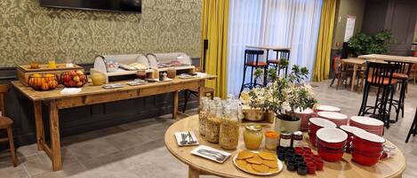 Mesa de desayuno buffet con diversos alimentos y un televisor fijado en la pared.