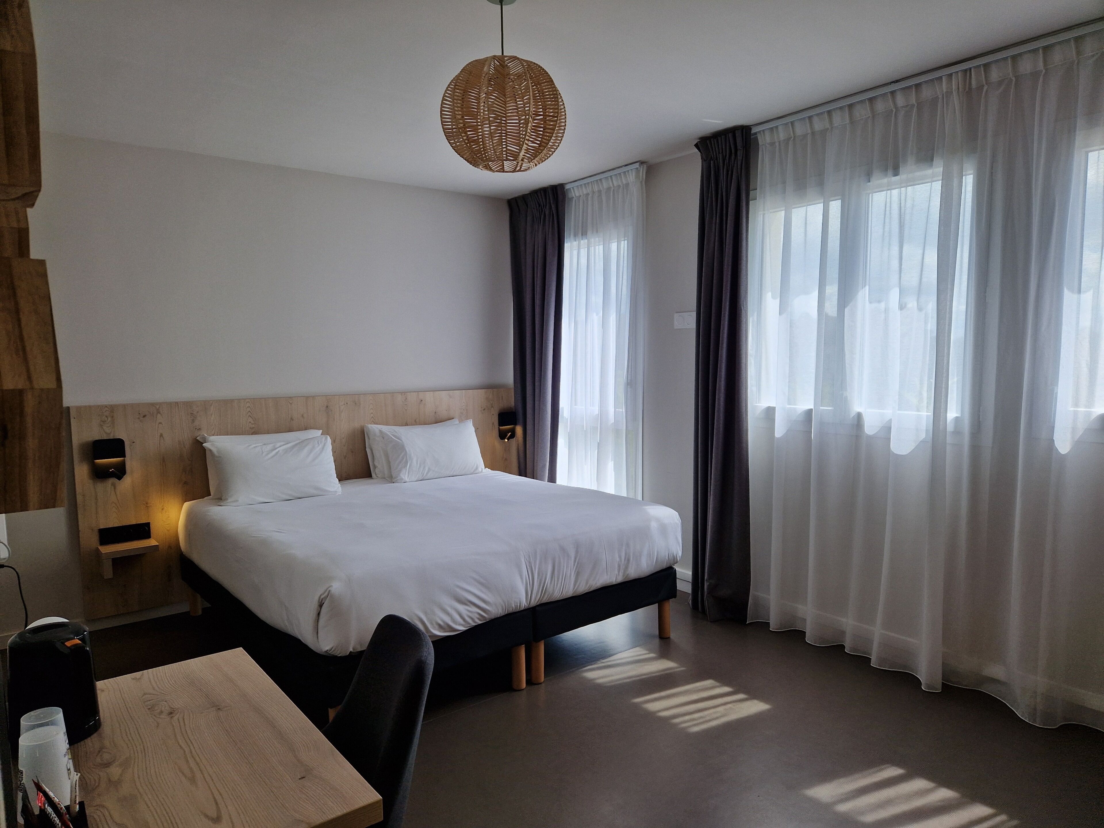 A modern hotel room with a large bed, wooden headboard, and a bedside table with a lamp.