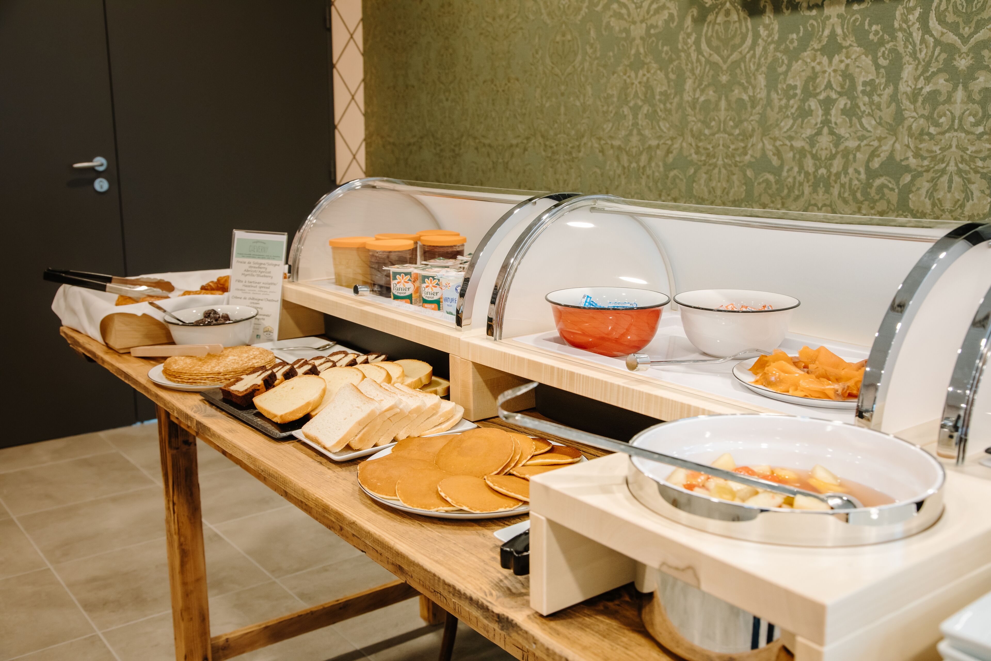 A buffet with various food items including pancakes, sandwiches, and fruit.