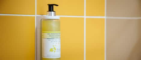 A bottle of gel douche argan shower gel mounted on a yellow tiled wall.