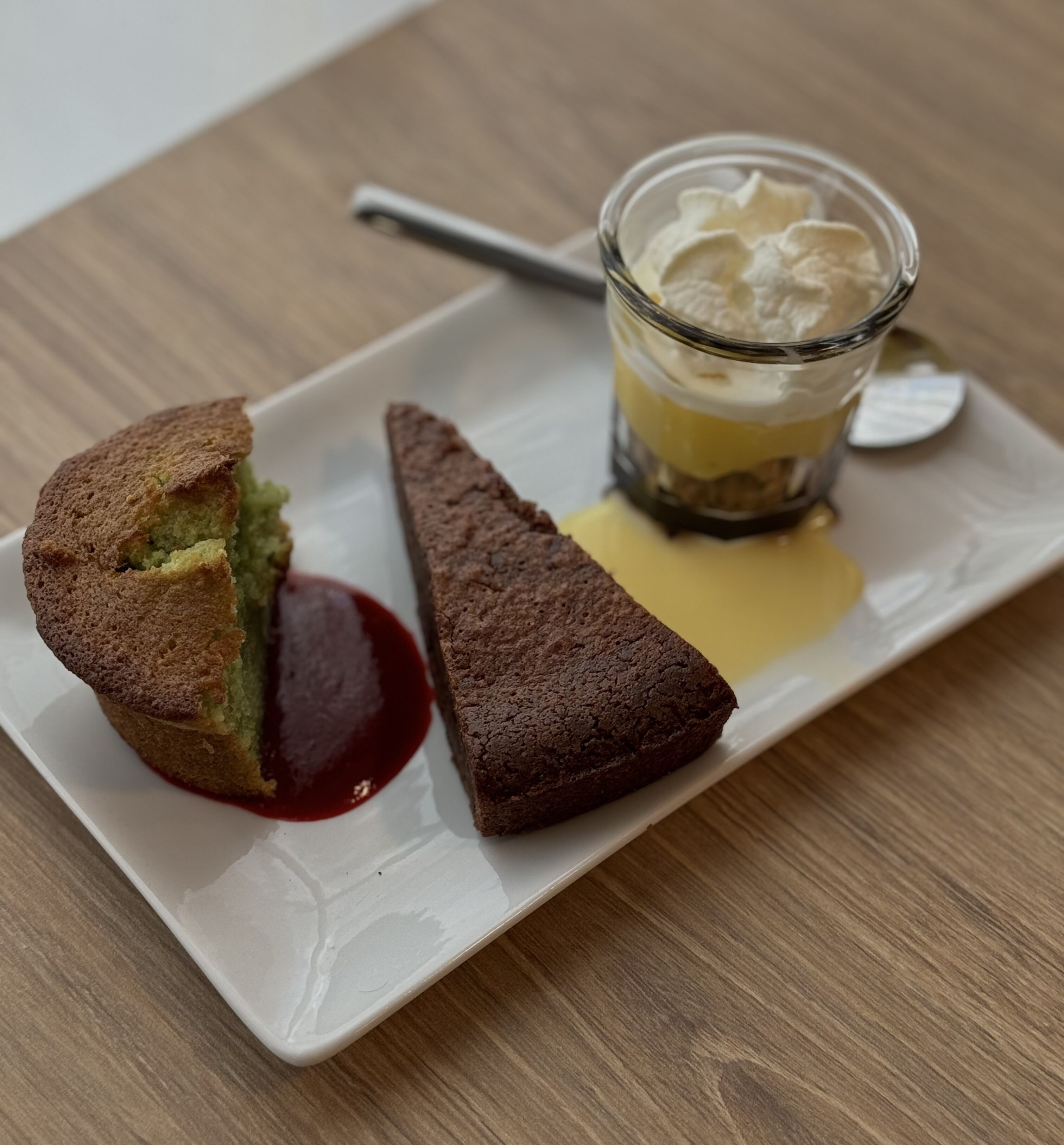 Jälkiruokalautanen, jossa on viipale kakkua, muffinssi ja kerroksittainen jälkiruoka lasissa.