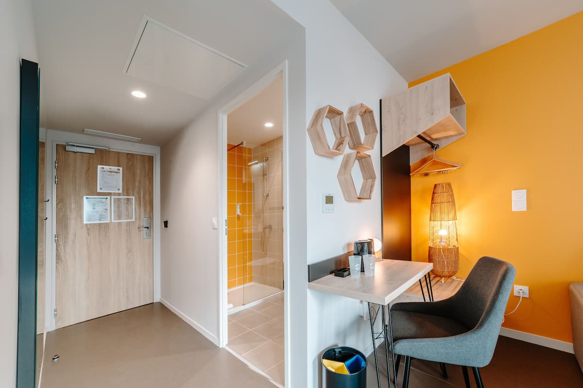 Une chambre d’hôtel moderne équipée d’une douche, d’une petite table avec une chaise et d’une lampe.