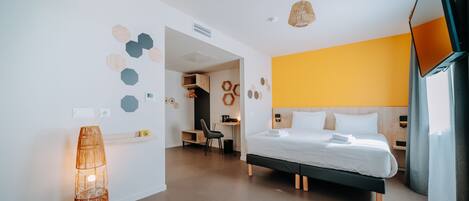 A modern hotel room with a bed, bedside table, lamp, and a view of the hallway.