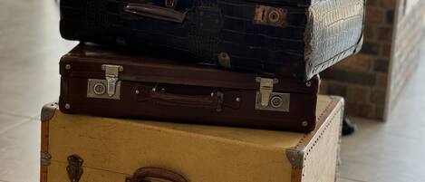 A stack of vintage suitcases in a room with a tiled floor and a brick wall.