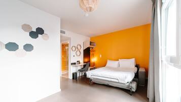 Una habitación de hotel moderna con cama, escritorio y silla. Hay una ventana con cortinas y una pared decorada con motivos hexagonales.