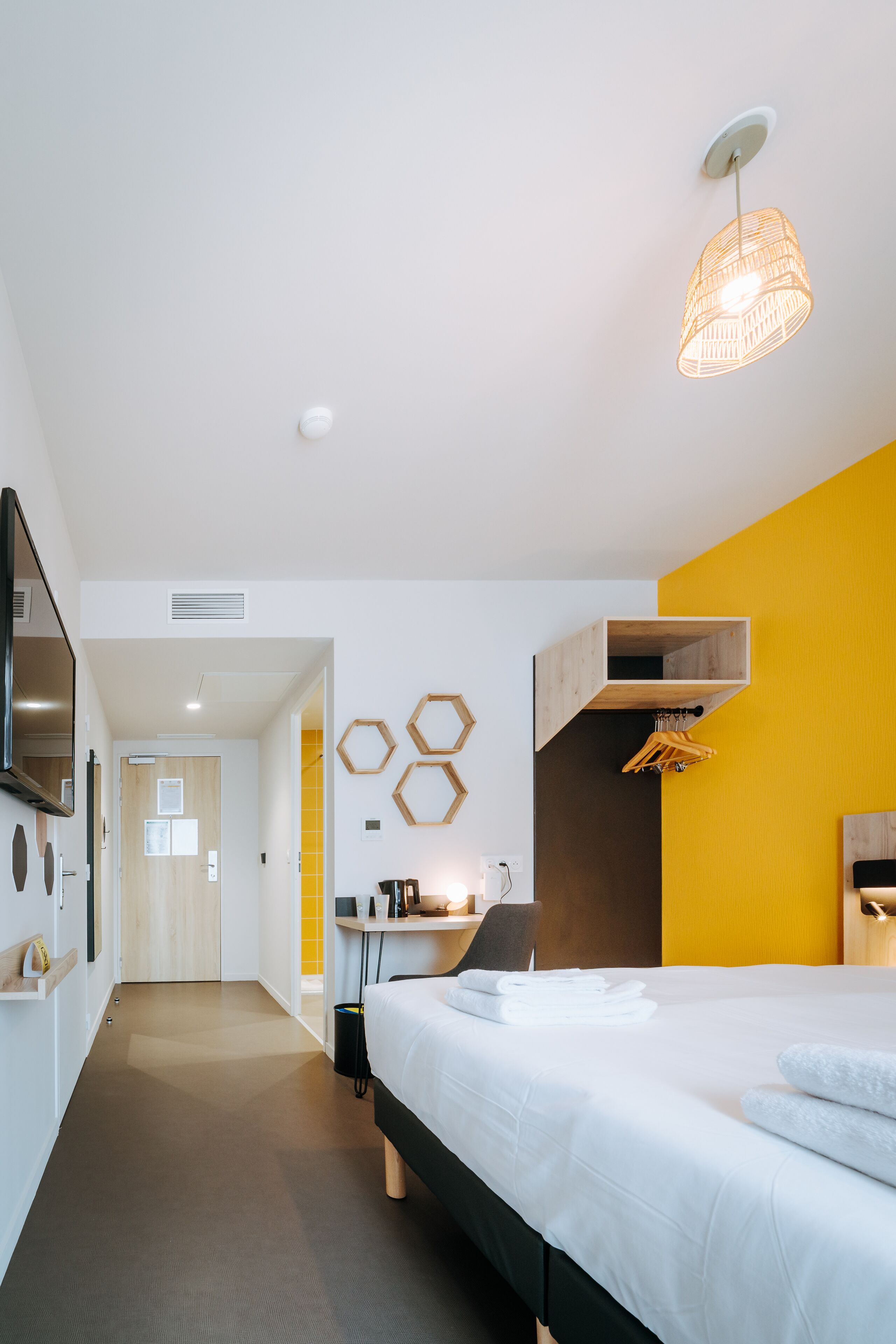 A modern hotel room with a bed, a desk, a chair, and a hanging light fixture.