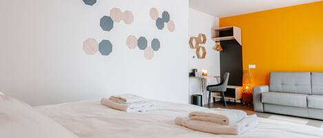 A modern hotel room with a large bed, a desk, and a sofa.
