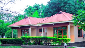 A two-story building with a red roof, large windows, and a well-maintained garden with hedges and a tree. - MIKUMI RESORT AND SAFARI HOTEL (Morogoro)