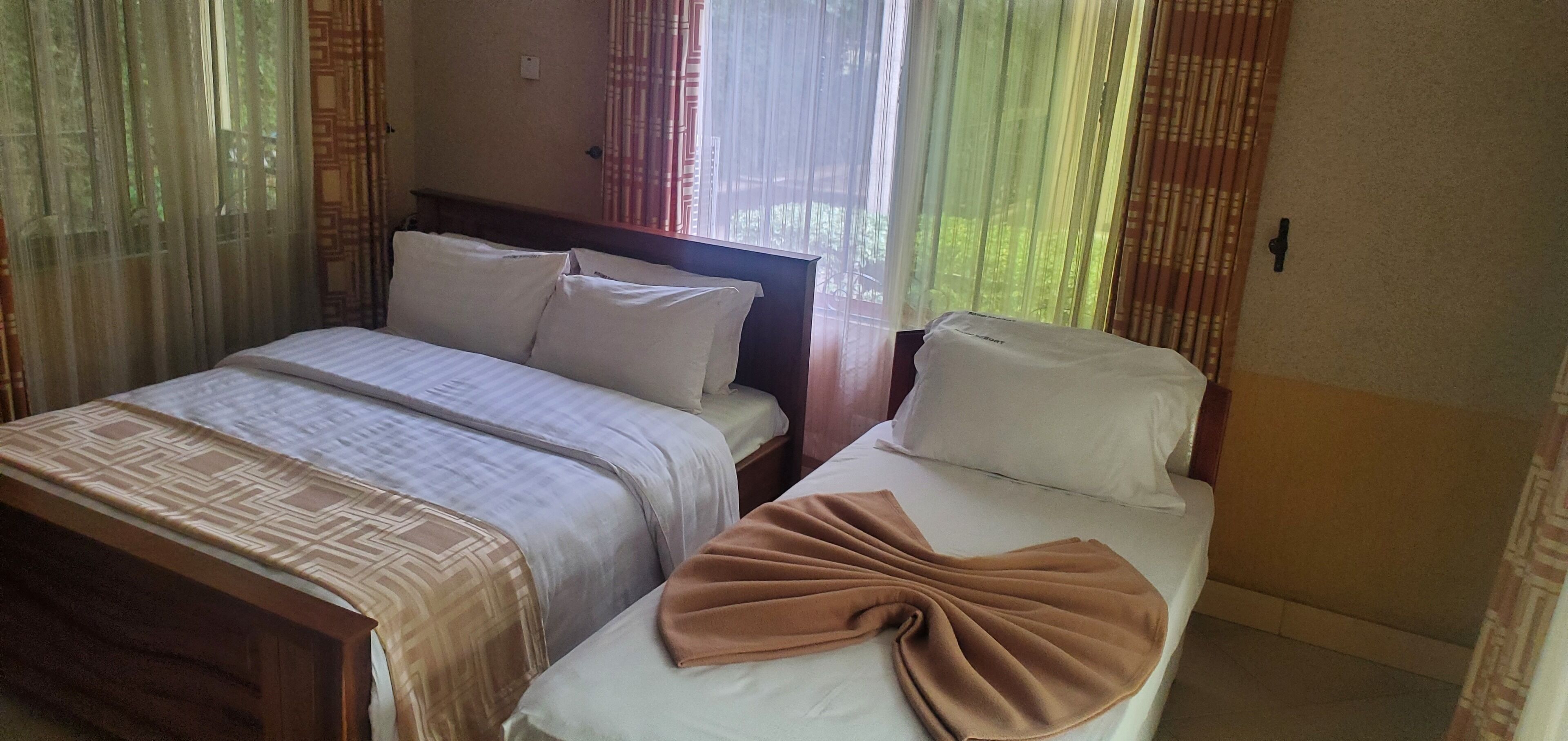A hotel room with two beds, a wooden headboard, and sheer curtains.