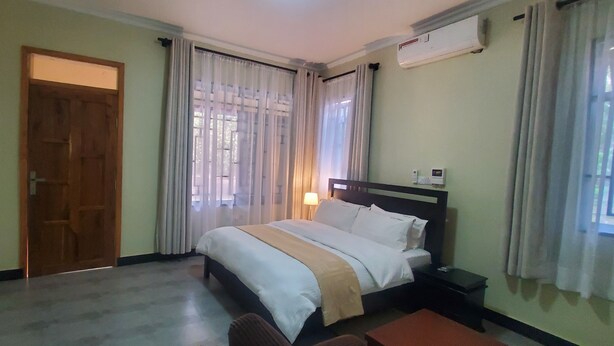 A hotel room with a bed, bedside table, and an air conditioning unit. - MIKUMI RESORT AND SAFARI HOTEL (Morogoro)