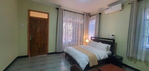 A hotel room with a bed, bedside table, and an air conditioning unit. - MIKUMI RESORT AND SAFARI HOTEL (Morogoro)