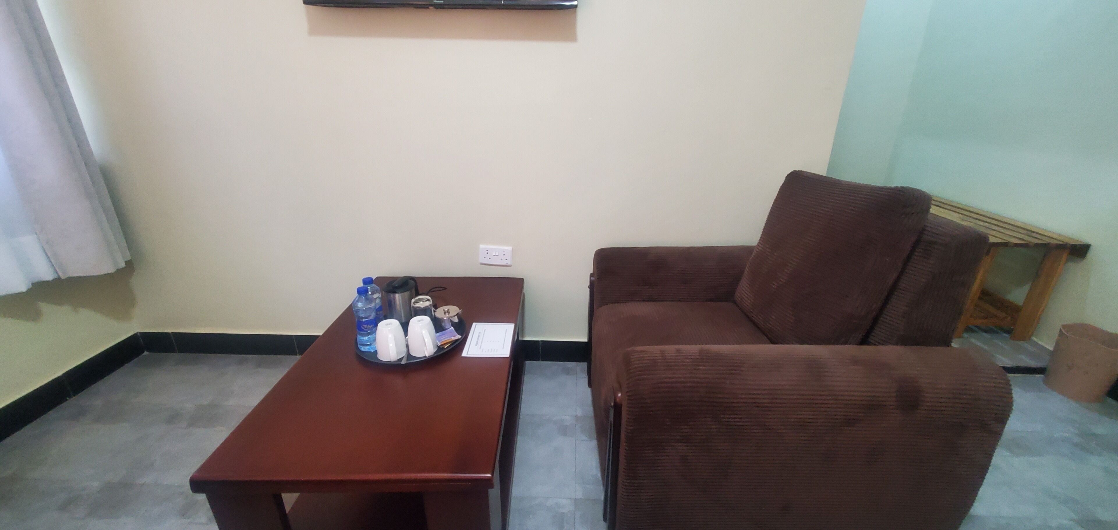 Una habitación pequeña con un sofá marrón y una mesa de madera. La mesa tiene una botella de agua, un termo y una taza. Hay un enchufe en la pared.