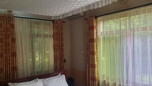 A room with a bed, large windows with sheer curtains, and a ceiling with a textured pattern. - MIKUMI RESORT AND SAFARI HOTEL (Morogoro)