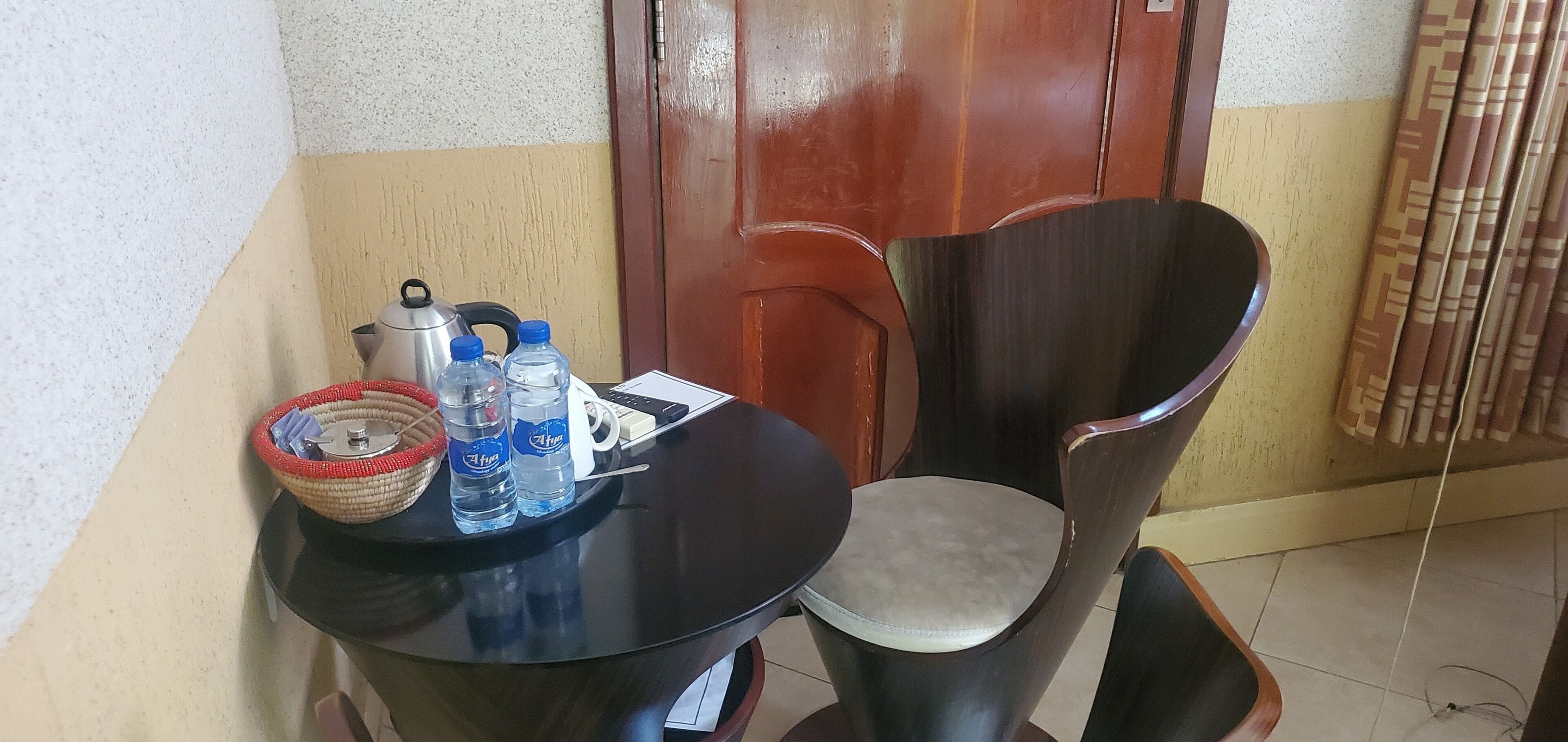 A small table with a basket, two water bottles, a kettle, and a remote control.