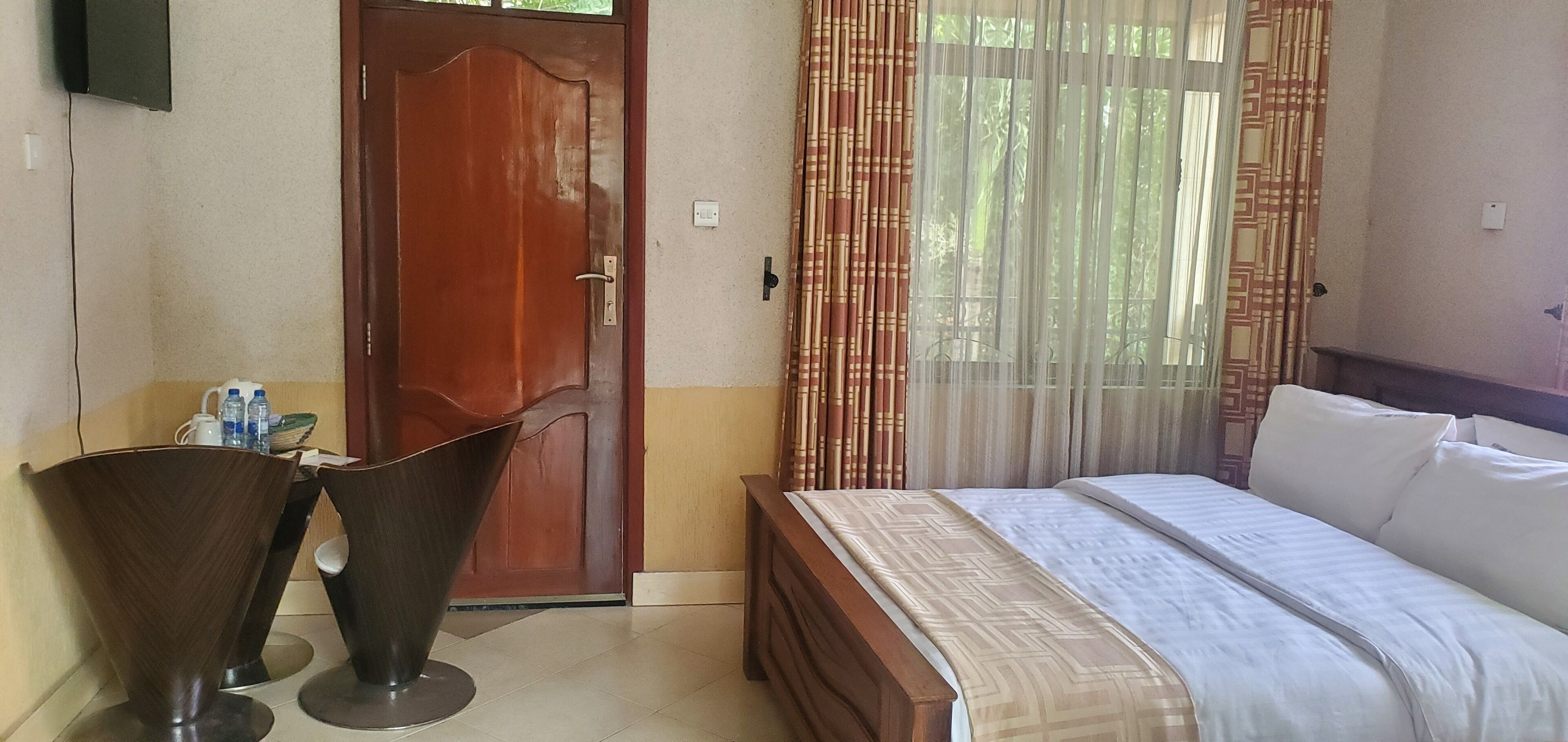 A bedroom with a bed, a wooden door, a small table with bottles, and a curtain.