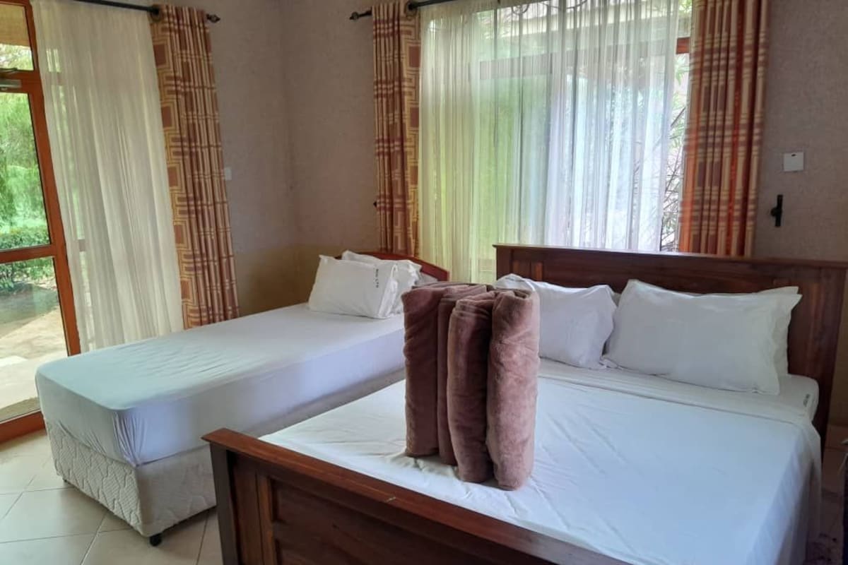A hotel room with two single beds, a wooden headboard, and a large window with curtains.