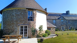 A stone building with a conical roof, a wooden bench, and a well-maintained lawn. - La Synchronicité - Chambres d'Hôtes (Saint-Sauveur-Villages)