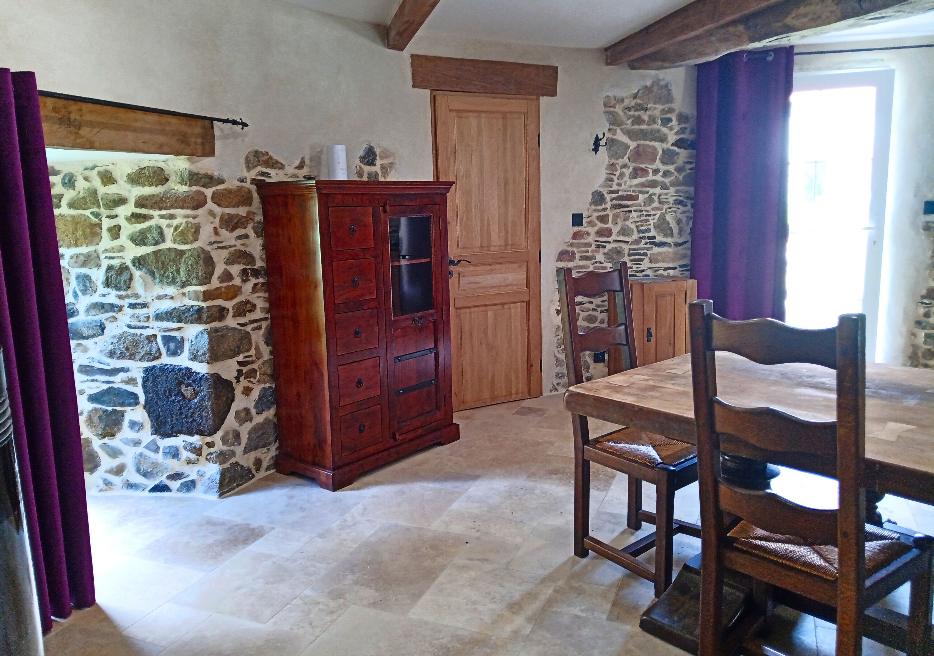 A rustic room with stone walls, a wooden cabinet, a dining table with chairs, and a door.