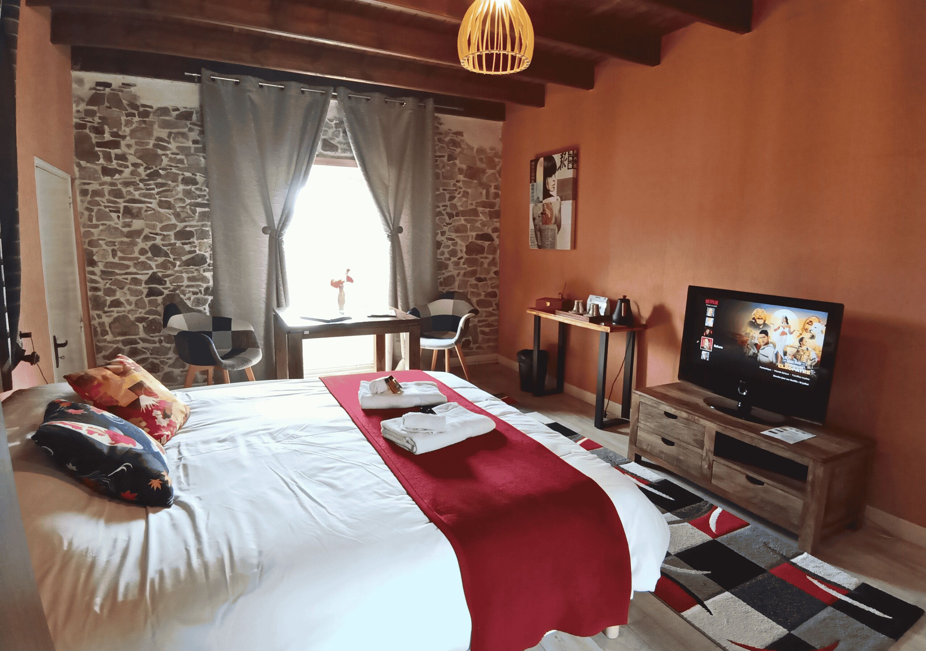 A hotel room with a bed, a TV, a desk, and a stone wall.