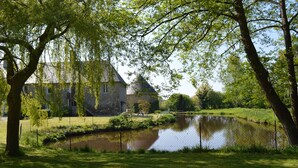 A stone building with a pond in front, surrounded by lush greenery. - La Synchronicité - Chambres d'Hôtes (Saint-Sauveur-Villages)